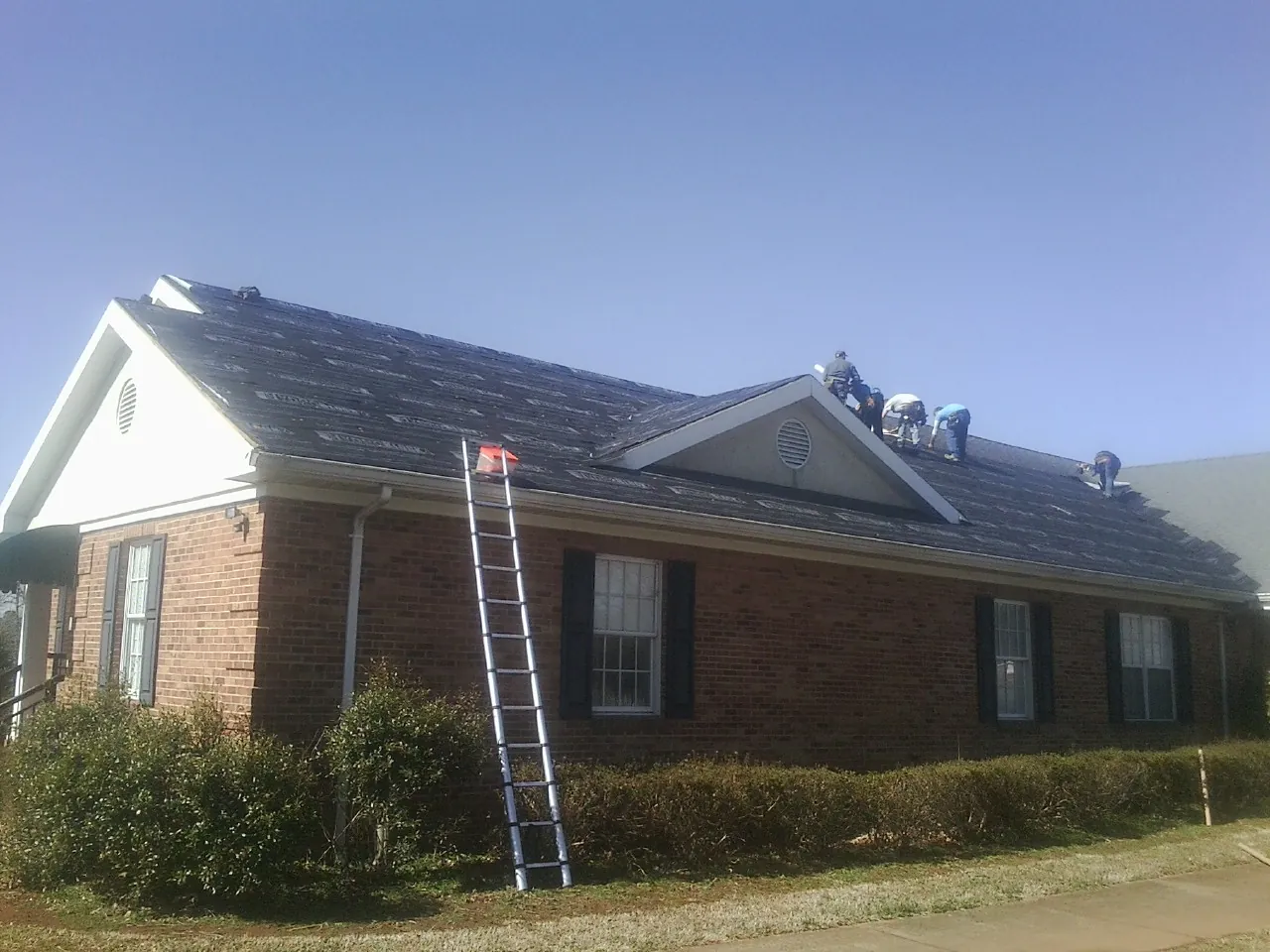 Crew tearing shingles off a brick ranch roof with a ladder set — Emergency Roof Repair work by our crew in Brodhead