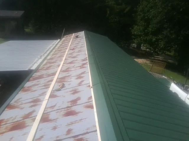 Old rusted panels beside newly installed green metal roofing — Wind Damage Roof Repair by Roofing Brothers in Brodhead