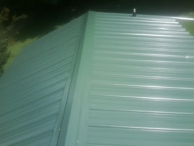 New green metal panels meeting at the ridge of a roof — Flat Roof Repair work by our crew in Brodhead